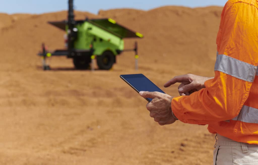 A man holding a tablet in front of a Mobile Solar Light Tower at a mine site.